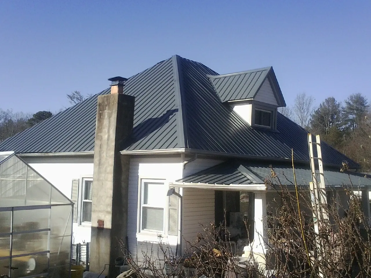 Dark blue standing seam metal roof on a white farmhouse with dormer — Slate & Tile Roof Repair by Roofing Brothers in Eaton